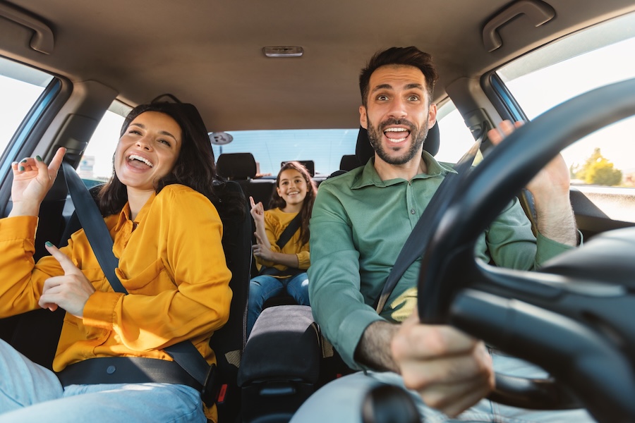 Happy family of three driving in their automobile, dancing to music and singing a favourite song, enjoying travelling by GoTo Flex Lease car